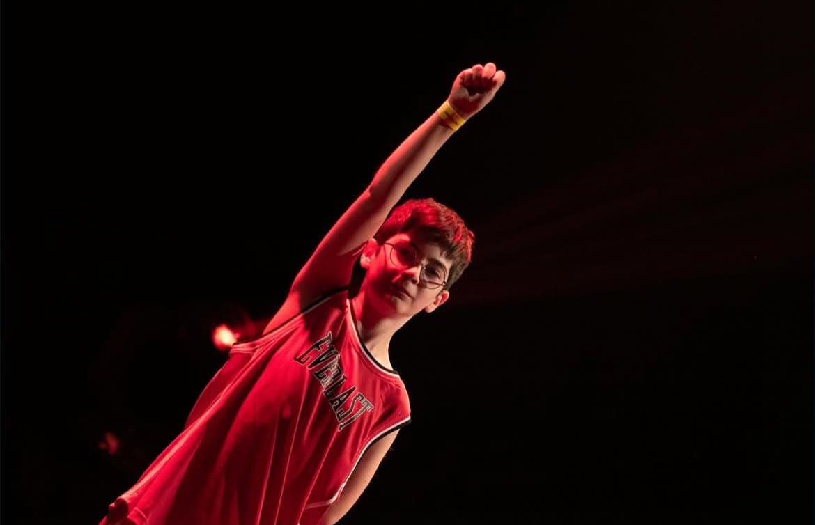 Young dancer in a red jersey with his fist raised on stage