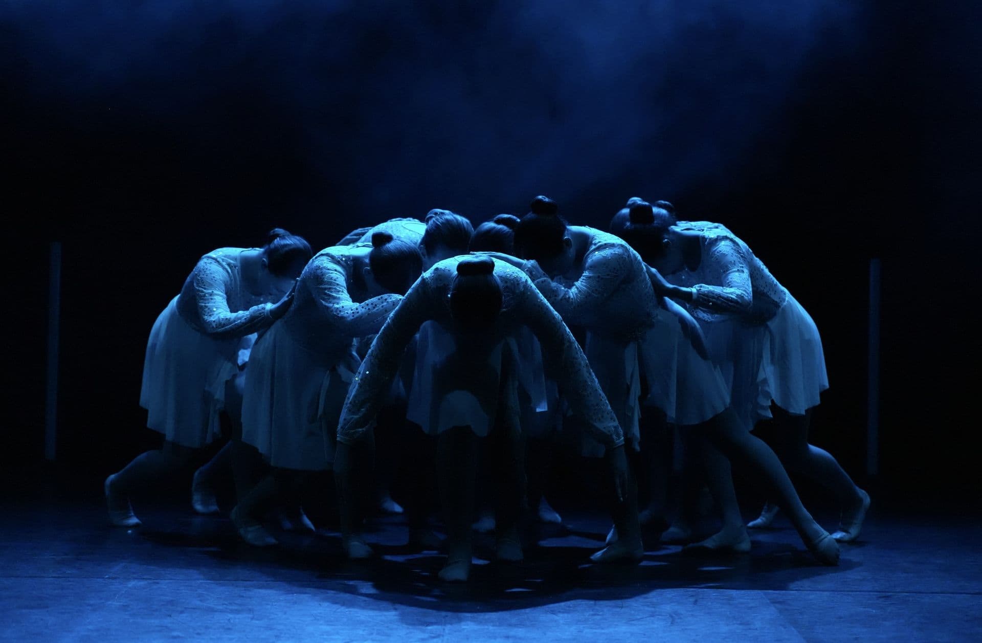 Contemporary dancers in a huddle on a blue stage