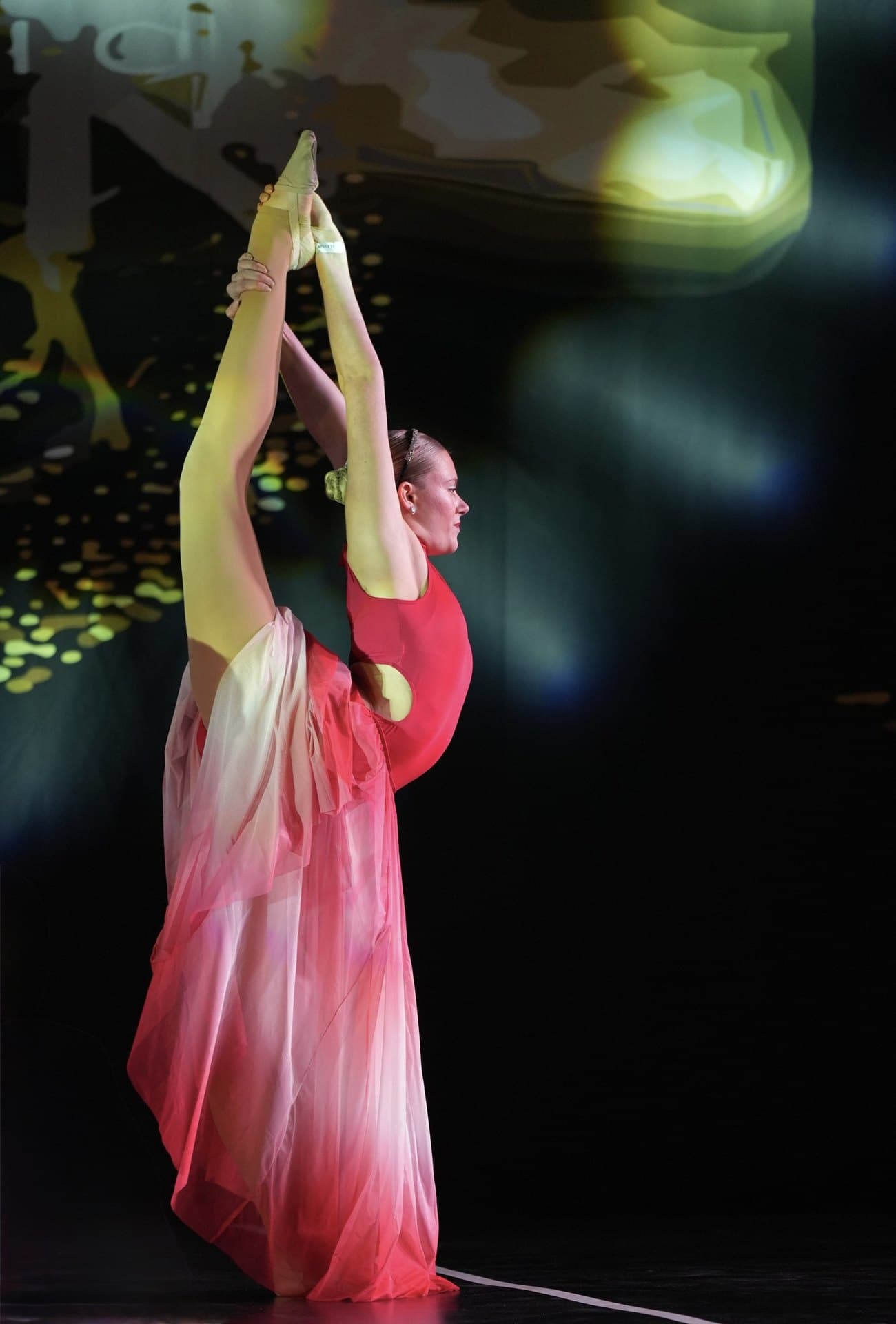 Lyrical dancer in a red ombre dress holding a standing split on stage